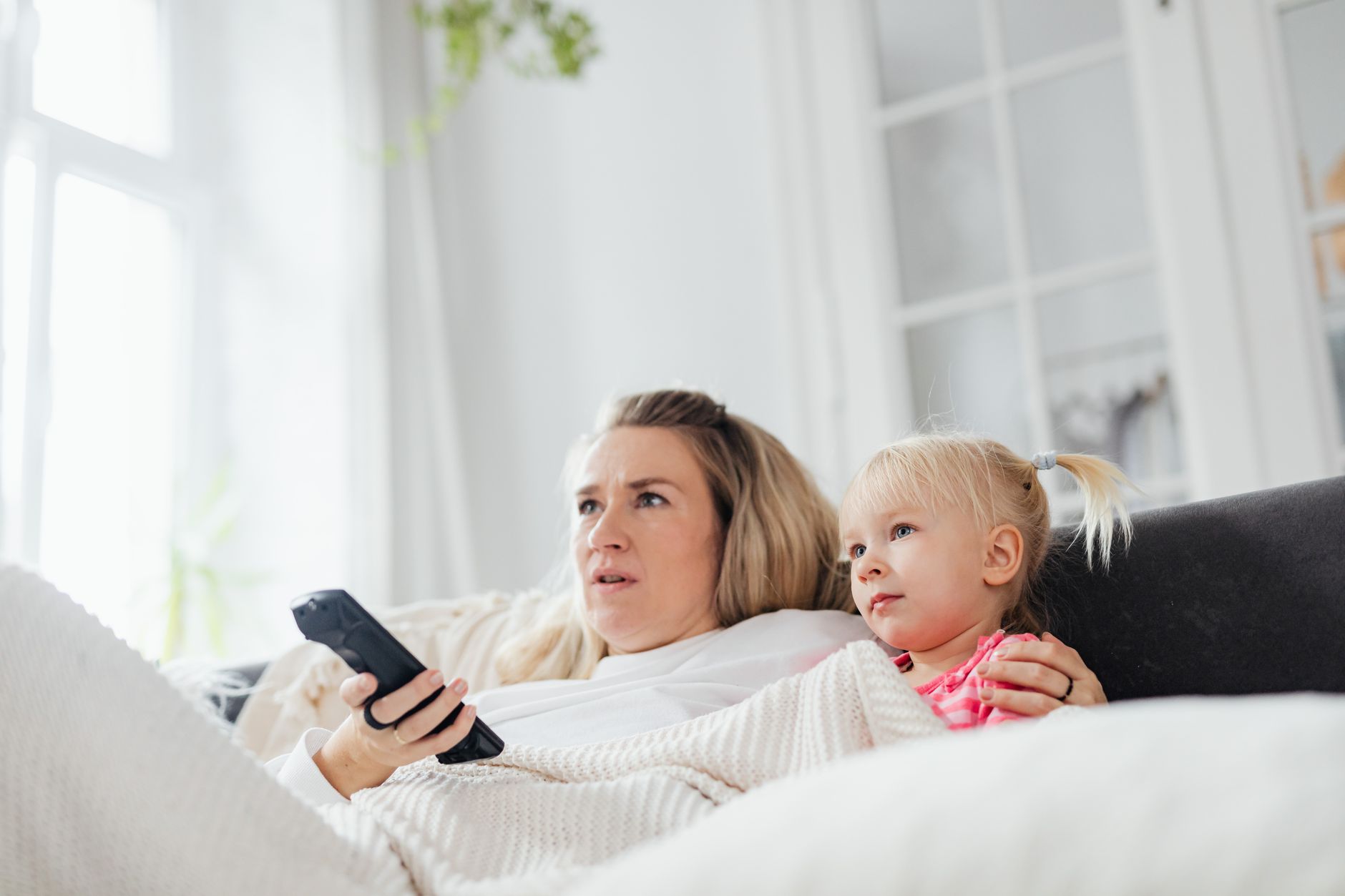 Zmęczona mama i córka odpoczywają razem na kanapie z pilotem